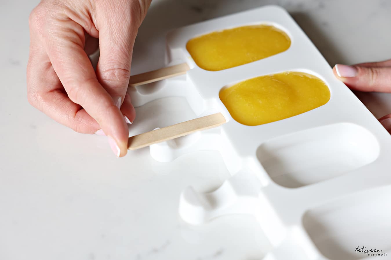 adding popsicle stick to mango sorbet in molds