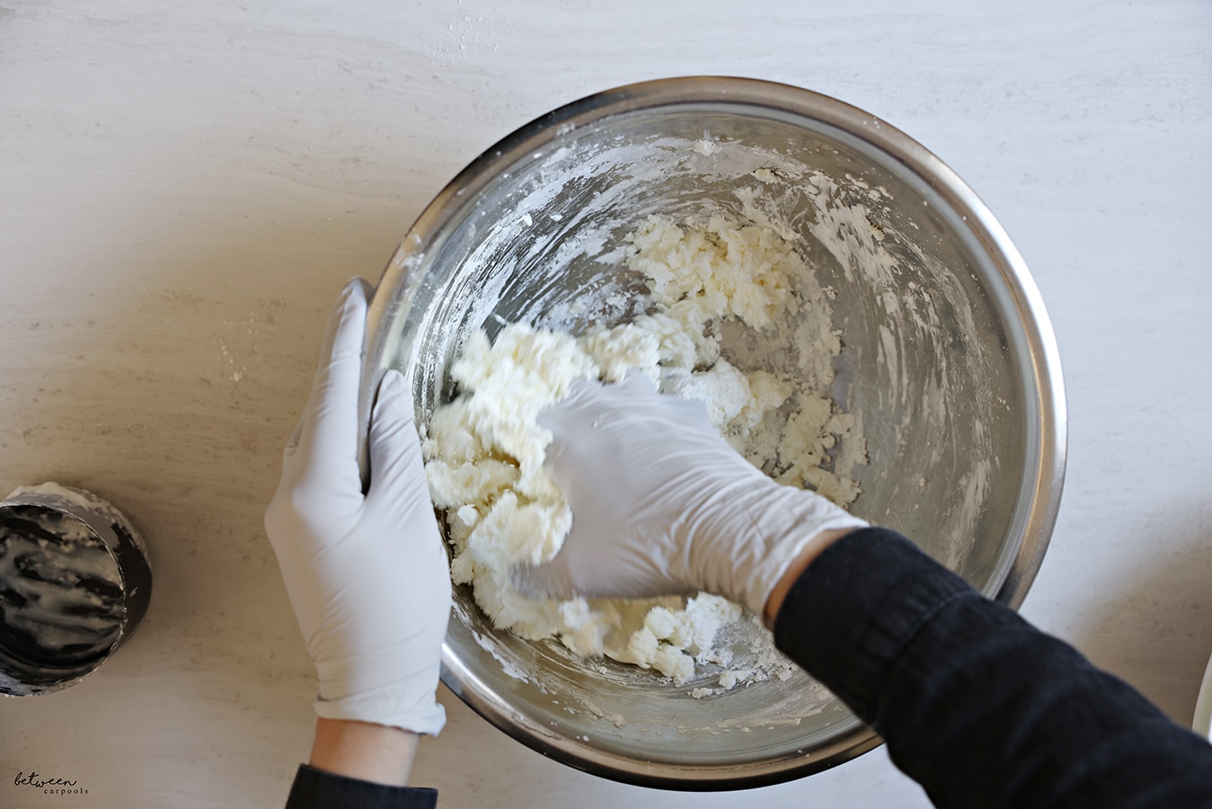 Mixing (with a gloved hand) corn starch and conditioner in a metal mixing bowl
