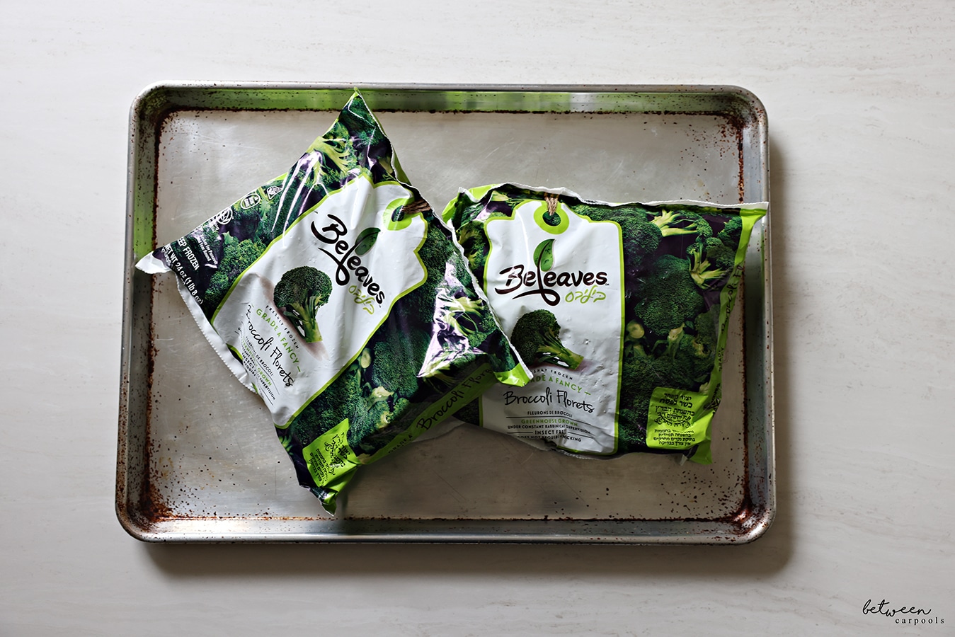 2 bags of broccoli florets on a large/big metal sheet pan