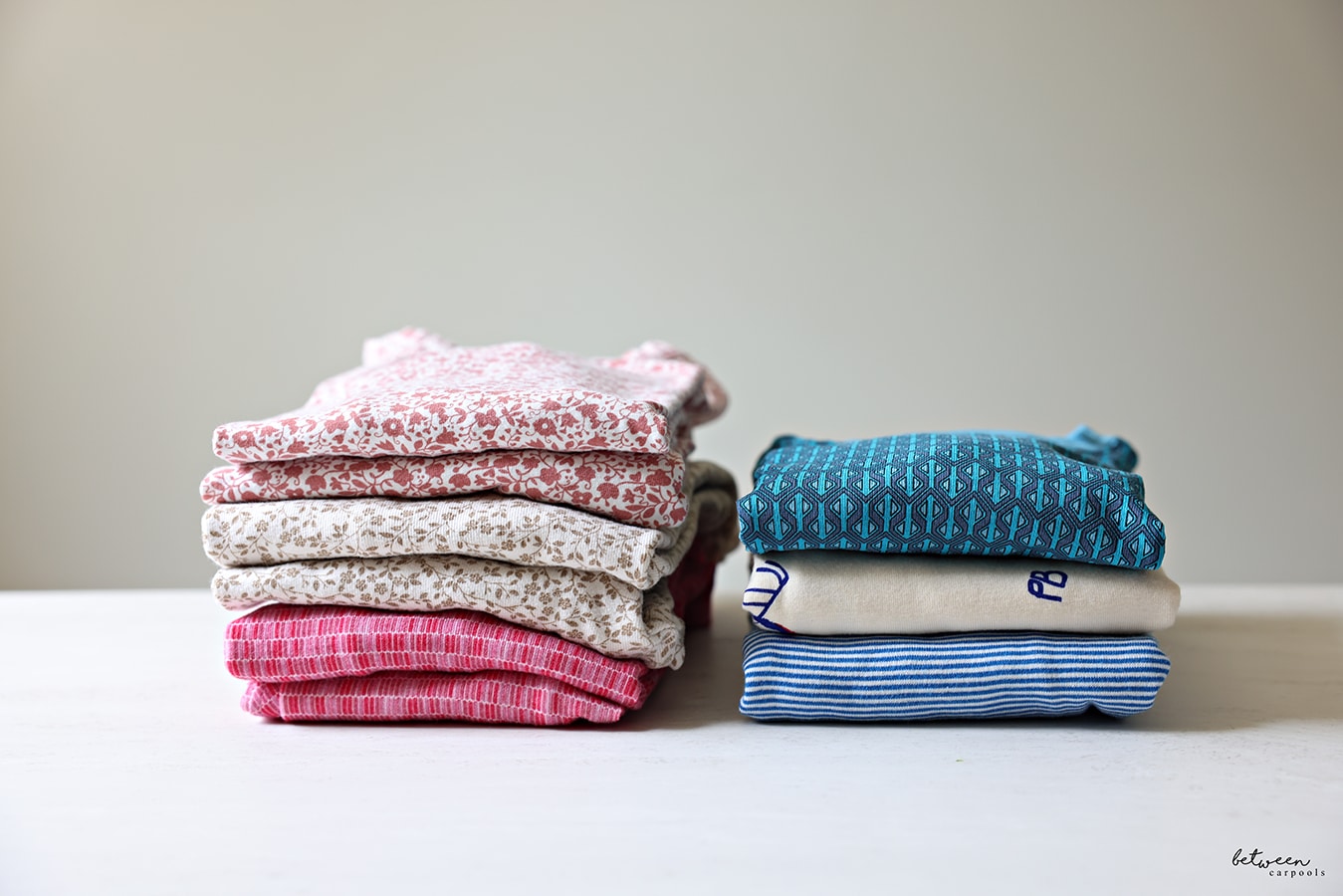 2 stacks of folded pajamas - pinks and blues - one folded traditionally (pants and shirts separate), and one folded as one piece (pants and shirts together).