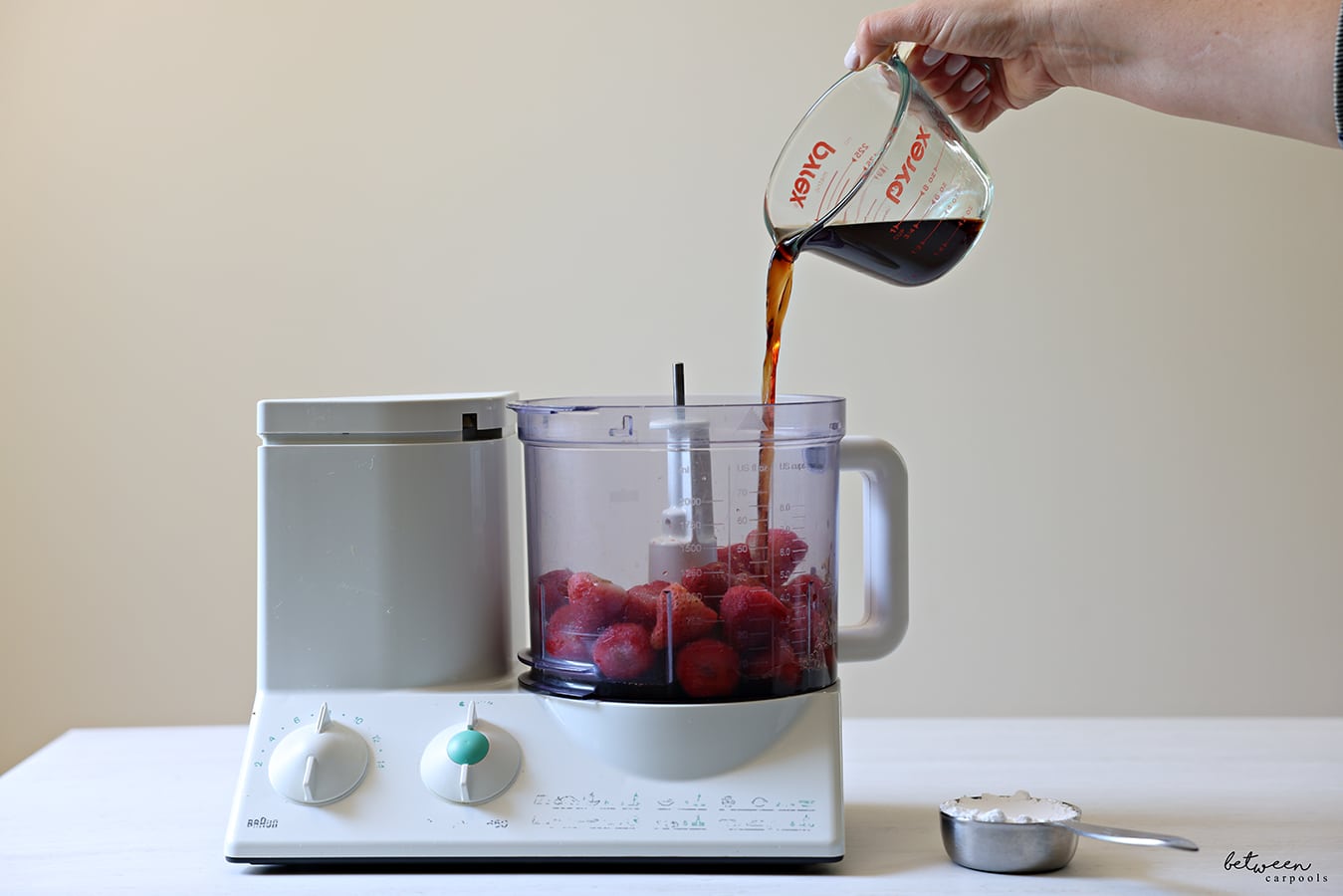 Pouring pomegranate juice into Braun food processor with frozen strawberries.