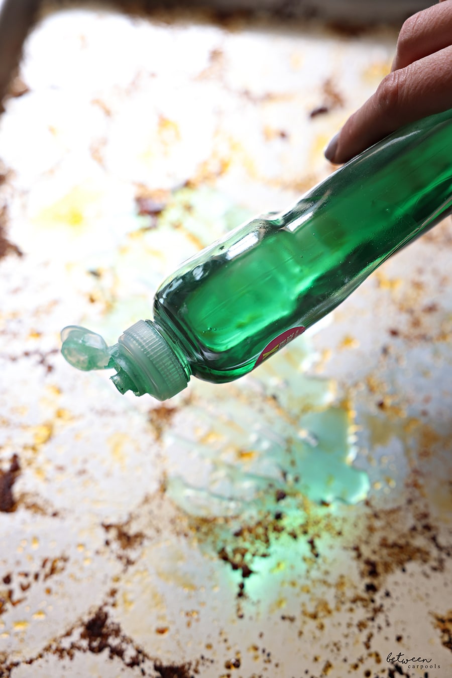 pouring dish soap on dirty metal sheet pan