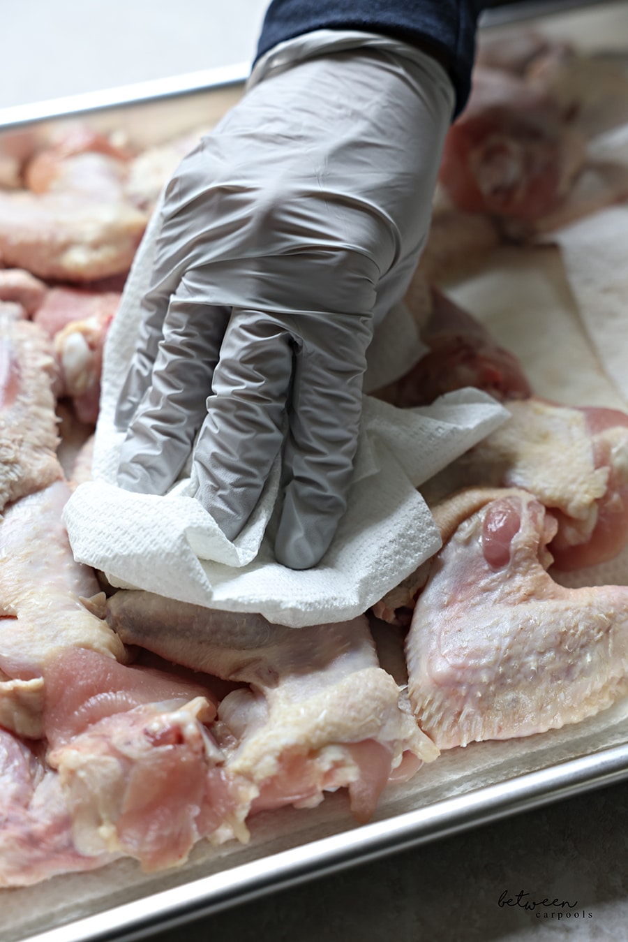 Drying chicken wings well with paper towel and a gloved hand.