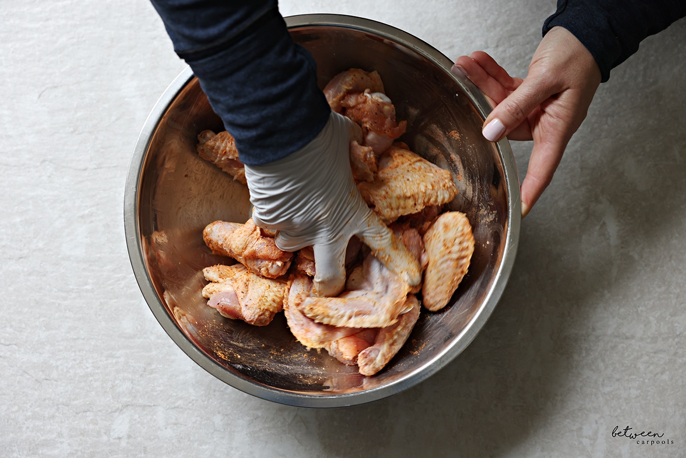 Tossing wings with all dry ingredients in a metal mixing bowl.