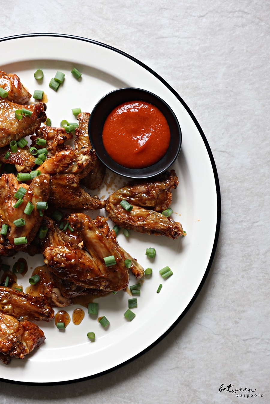Wings, plated - topped with scallions - and hot sauce