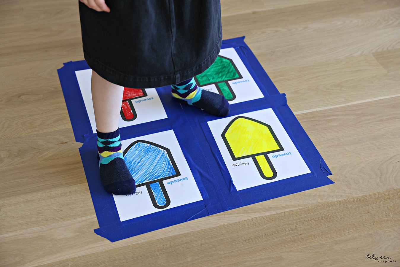 4 between carpools x toveedo dreidel downloads - colored yellow, blue, green, and red - taped to the floor, like a square, with blue tape.