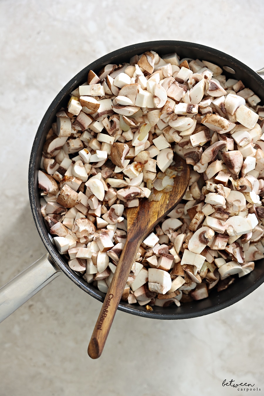 Diced white and baby bella mushrooms, sautéed onion and garlic in a sauté pan with a wooden spoon.