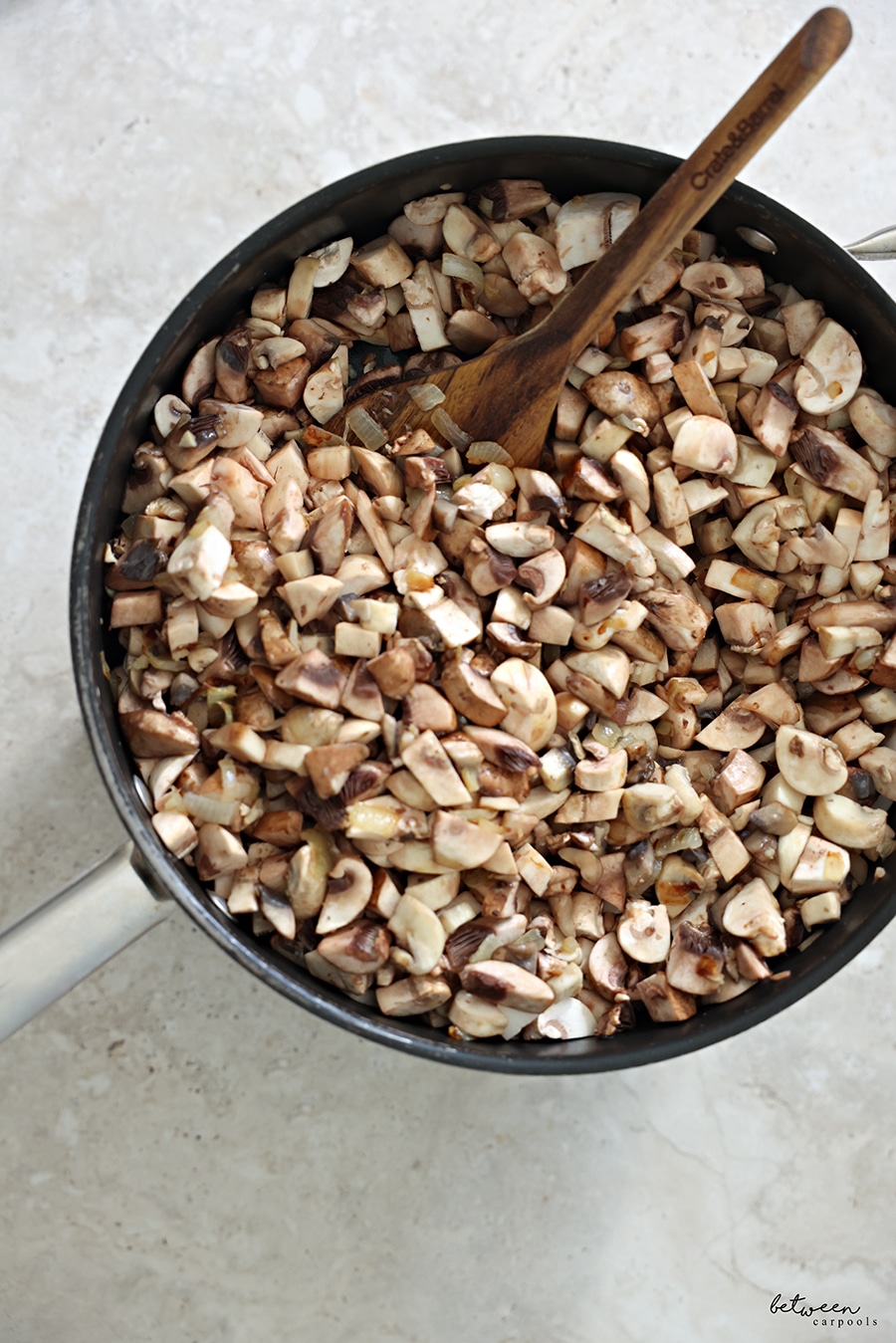 Diced and golden white and baby bella mushrooms, sautéed onion and garlic in a sauté pan with a wooden spoon.