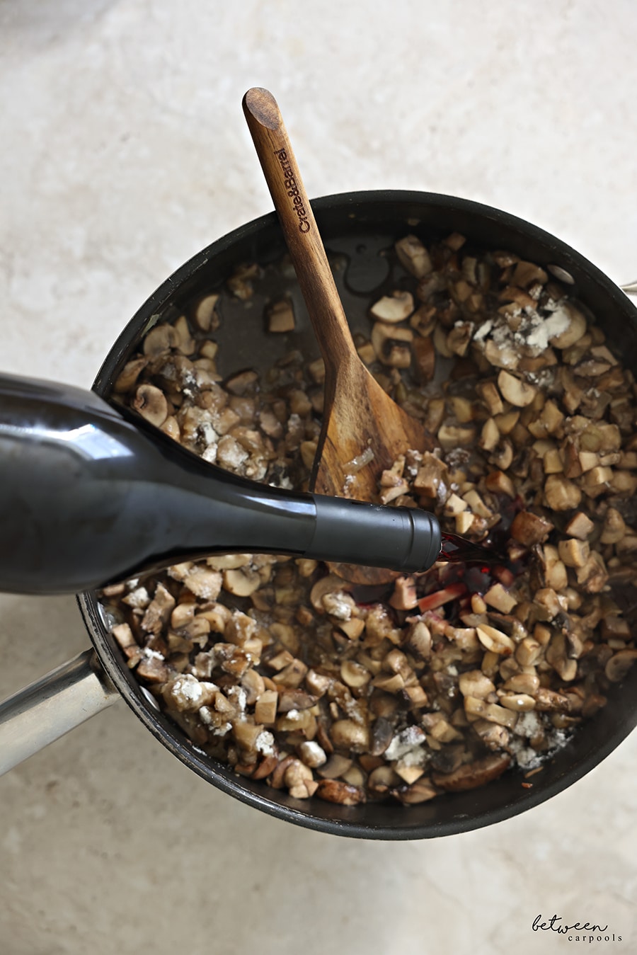 Adding red wine to sautéed onion, garlic, white and baby Bella mushrooms + flour in a sauté pan with a wooden spoon.