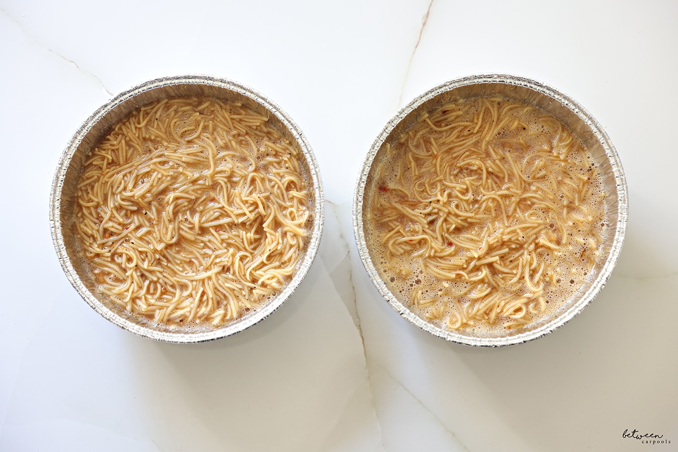 Two round aluminum pans with Yerushalmi Kugel mixture on a kitchen counter.