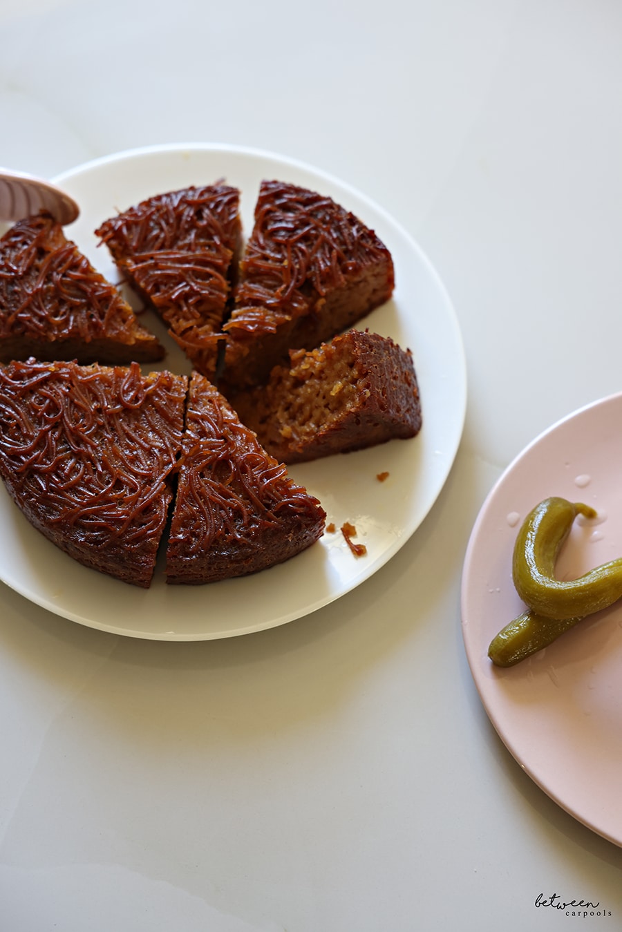 Yerushalmi Kugel, sliced, on a plate. Israeli pickles on another plate.