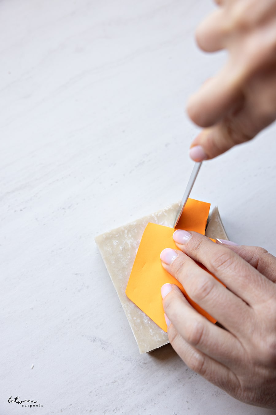 Using a paper dreidel shape to cut dreidel shapes out of a stack of wonton wrappers.