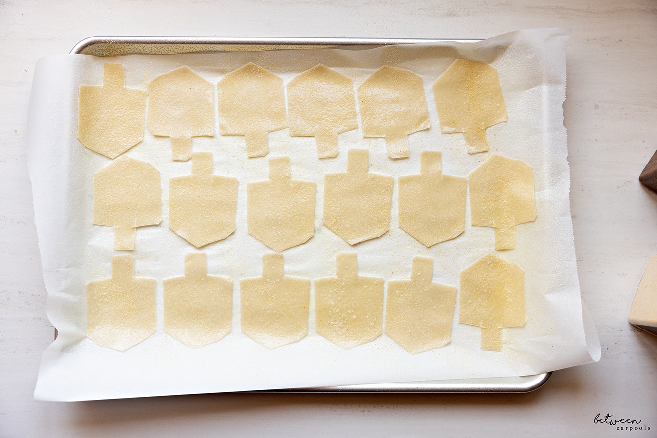Dreidel shape wonton wrappers, with salt and garlic powder, on a parchment lined baking sheet.