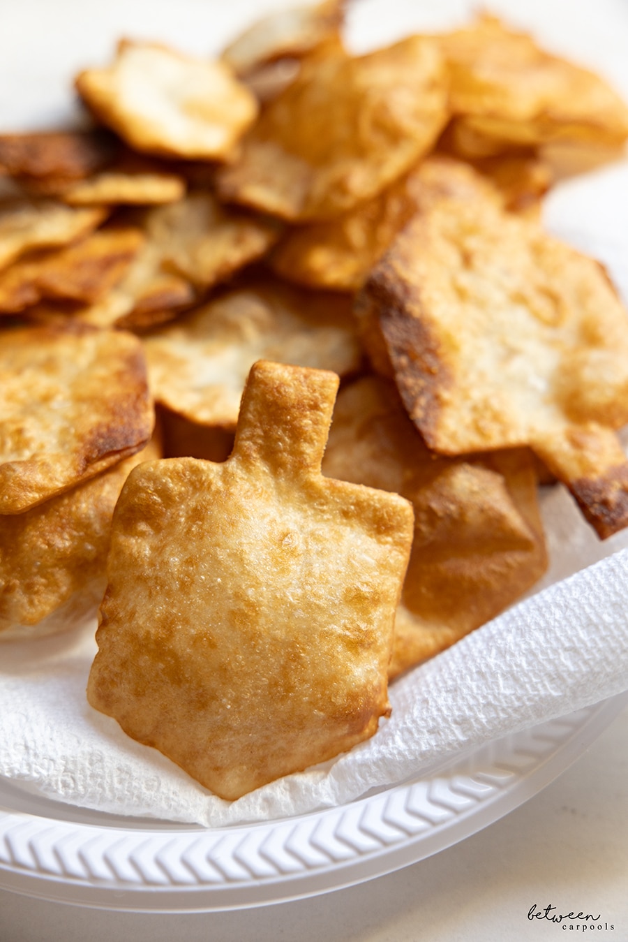 Closeup of dreidel shape wraps and wontons on a paper towel lined plastic plate.