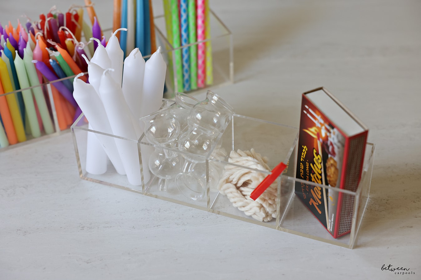 4-section acrylic organizers, filled. One with colored candles and one with Shabbos candles, Menorah oil glasses, wicks (plus a plastic tweezer) and a box of matches.