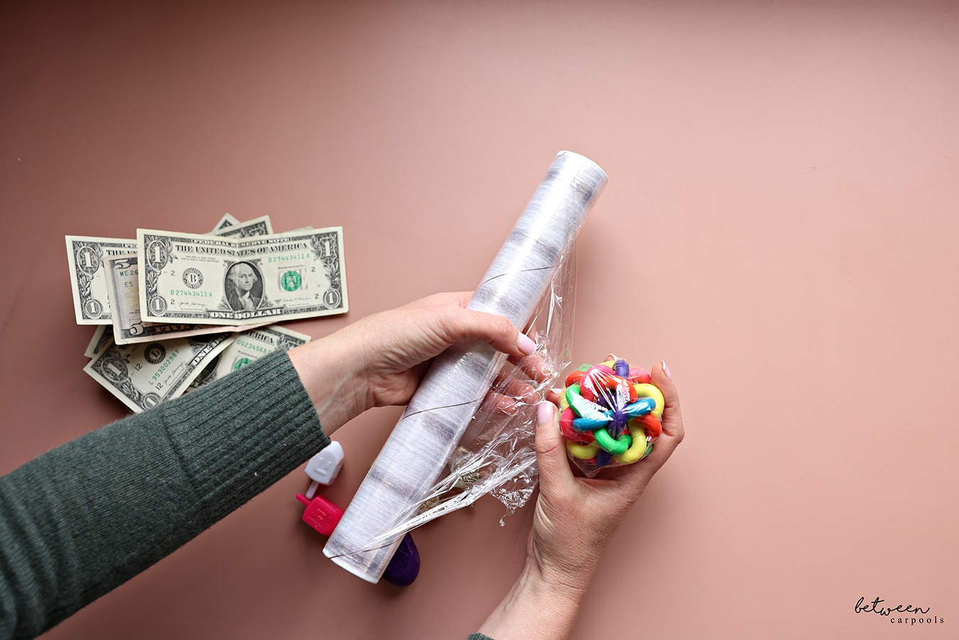A small ball wrapped in Saran Wrap in her right hand. The roll of Saran Wrap in her left hand. Money and dreidels nearby.