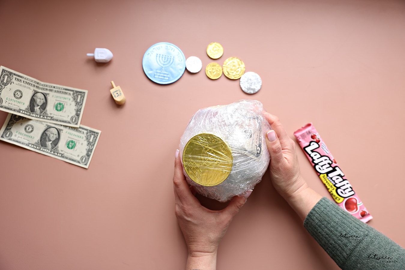 Holding a complete prize ball in both hands. Lafffy Taffy, chocolate coins, dreidels and dollar bills nearby.