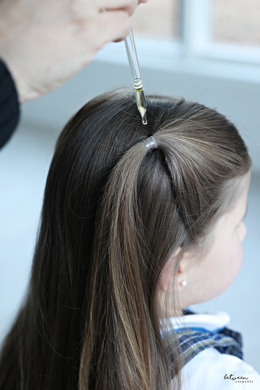 Adding a drop of lemon oil to a ponytail on a little girl.