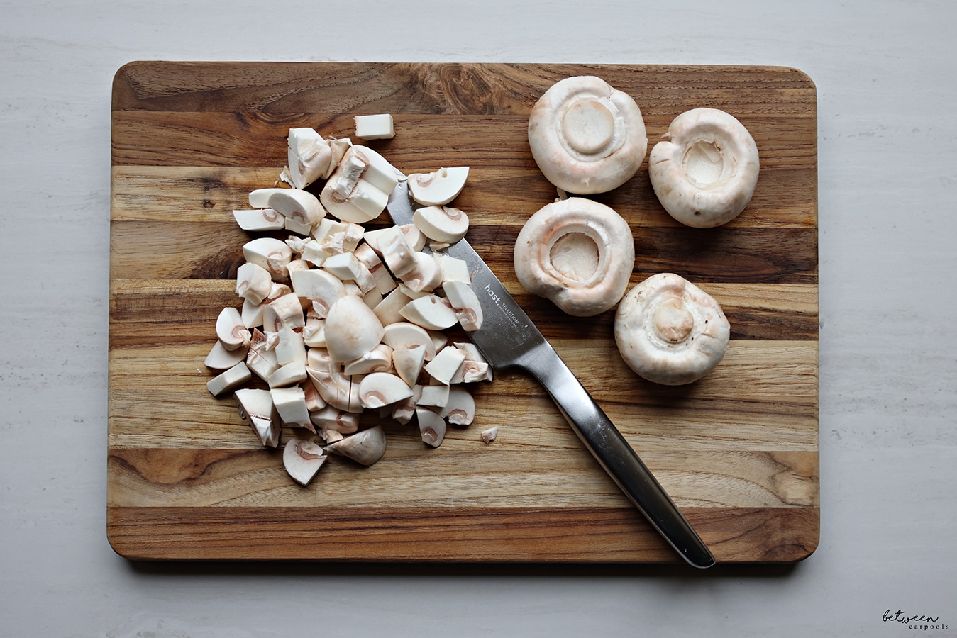 Whole and sliced white mushrooms on a wooden cutting board with knife.