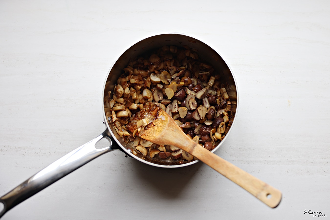 Sautéed onions, white mushrooms, garlic, sliced chestnuts and white wine in a saucepan with a wooden spatula.
