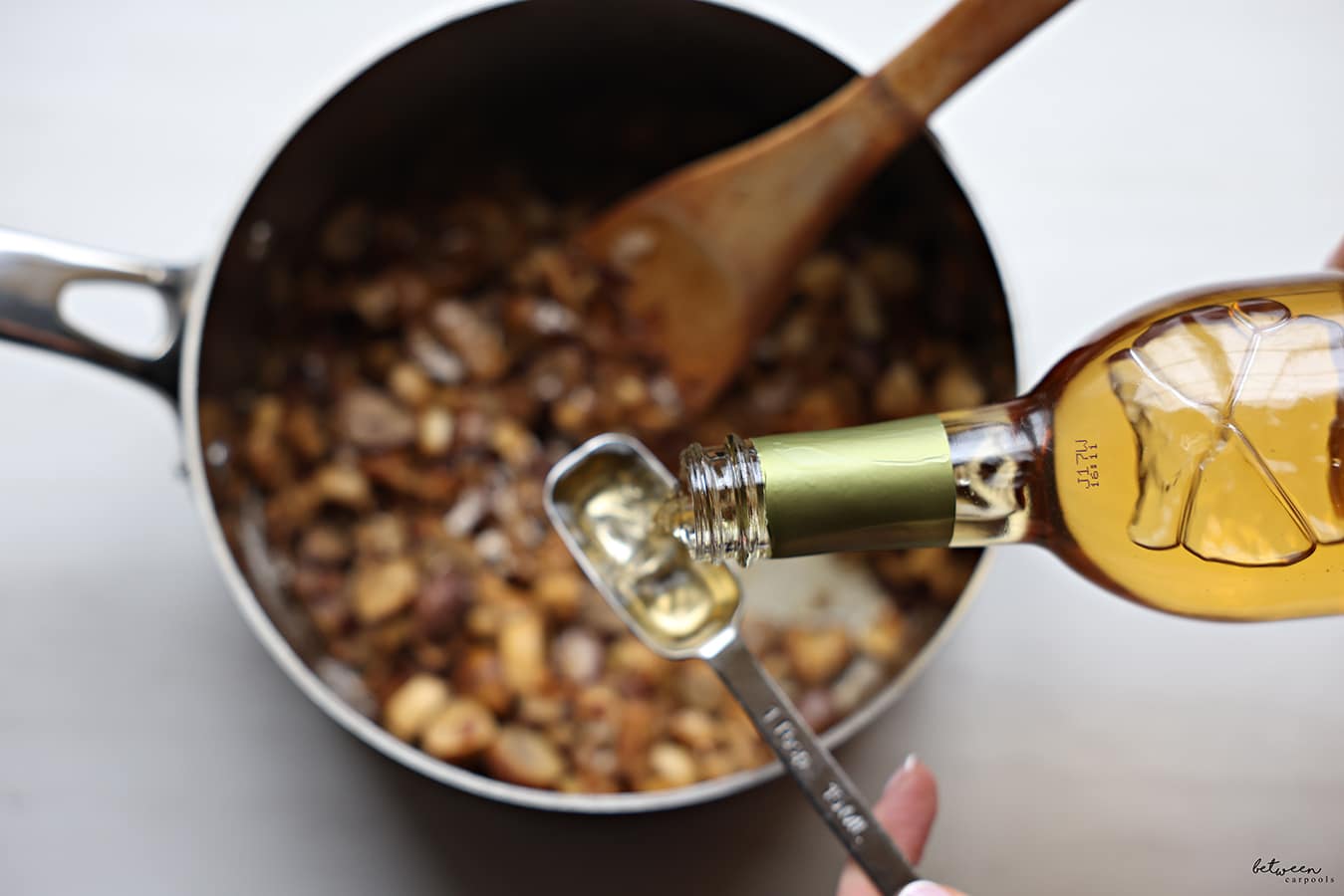 Adding white wine to sautéed onions, white mushrooms and garlic in a saucepan with a wooden spatula.