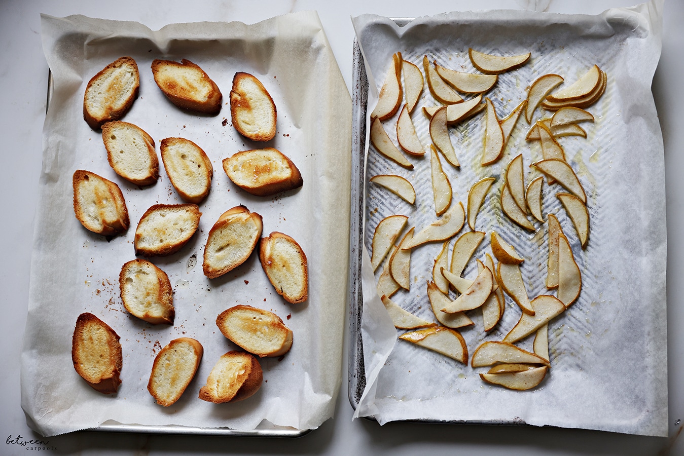 Bruschetta and roasted pear slices on parchment lined metal sheet pans.