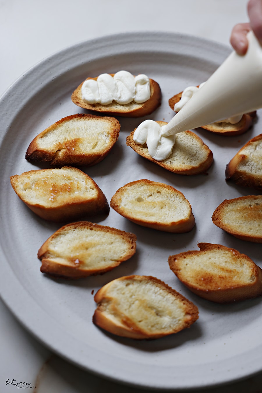 Piping ricotta cream onto bruschetta - toasted baguette slices.