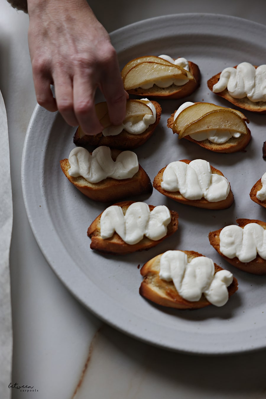 Laying a couple of roasted pear slices on top of bruschetta with ricotta cream.