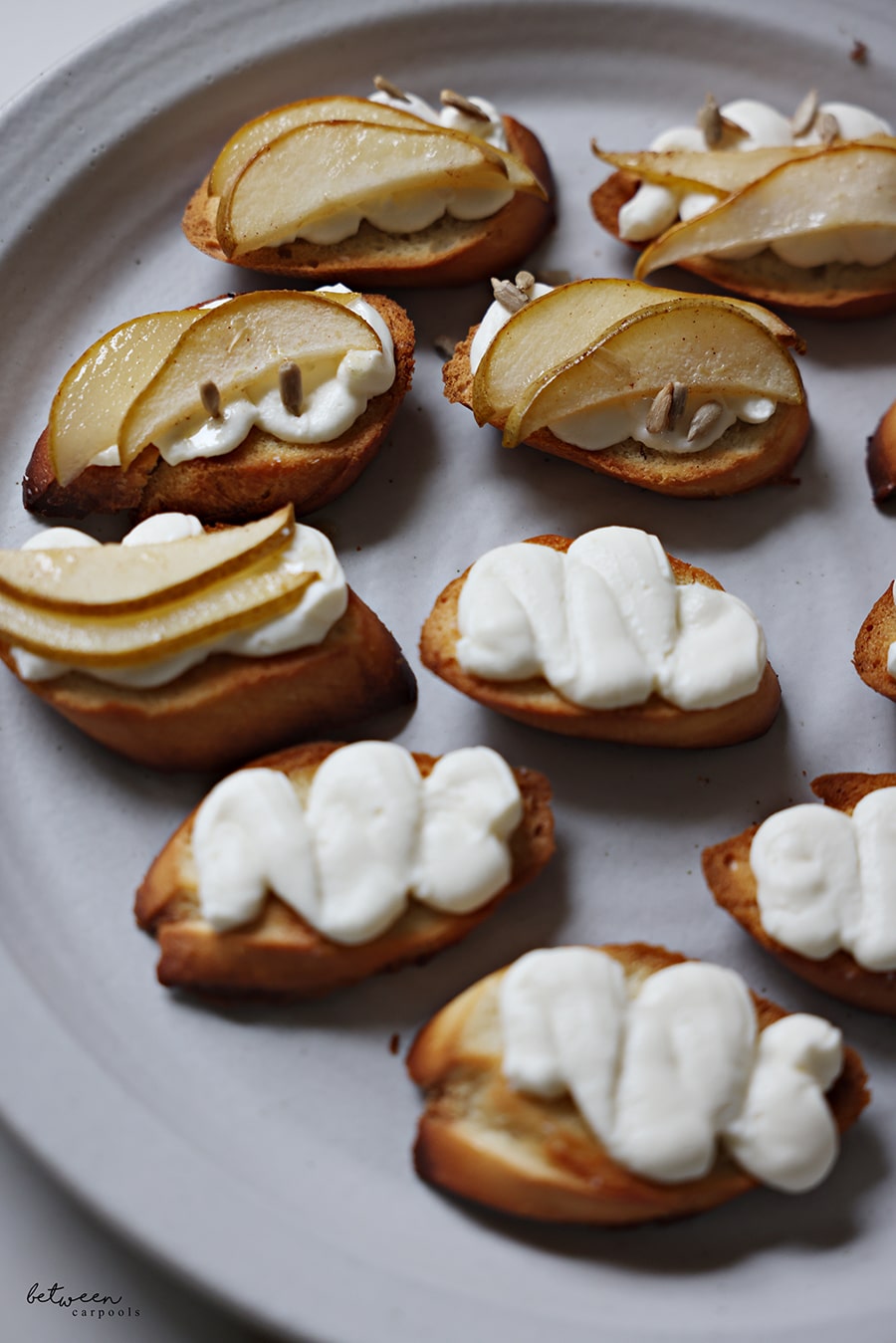 Bruschetta with ricotta cream, roasted pear slices, and sunflower seeds.