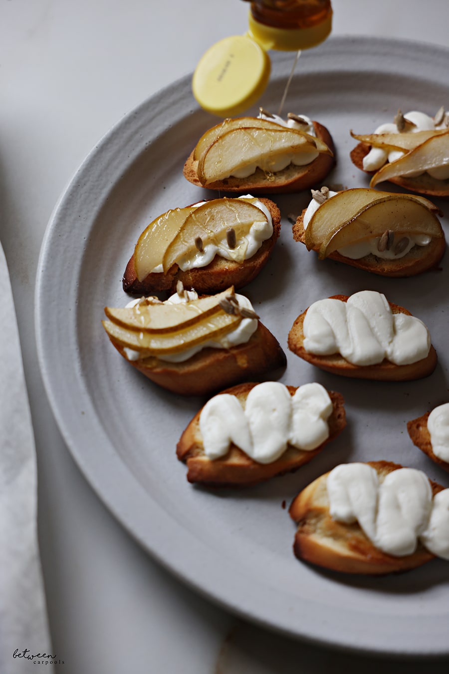 Drizzling honey on bruschetta with ricotta cream, roasted pear slices, and sunflower seeds.