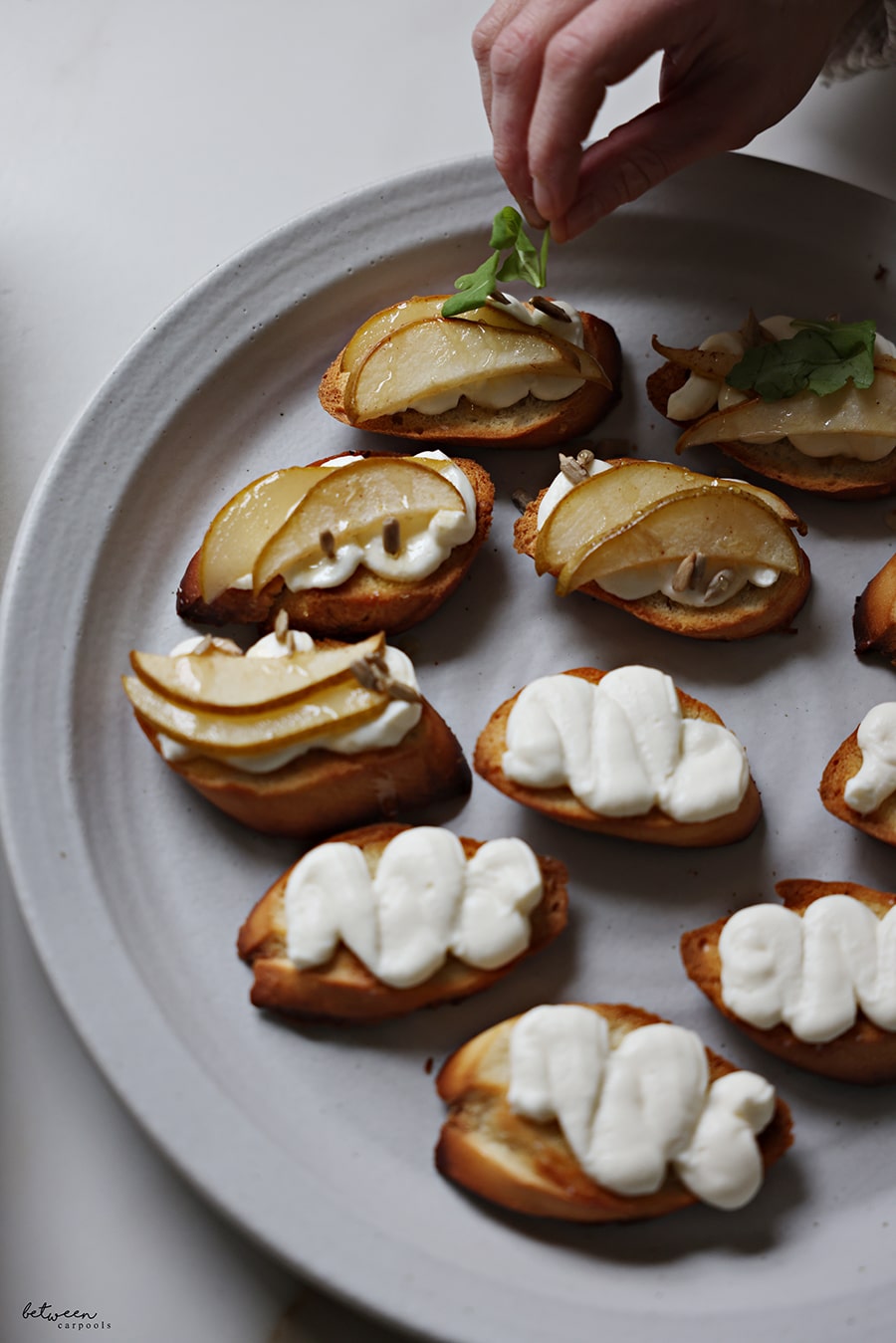 Adding a spring of arugula on bruschetta with ricotta cream, roasted pear slices, sunflower seeds and a drizzle of honey.
