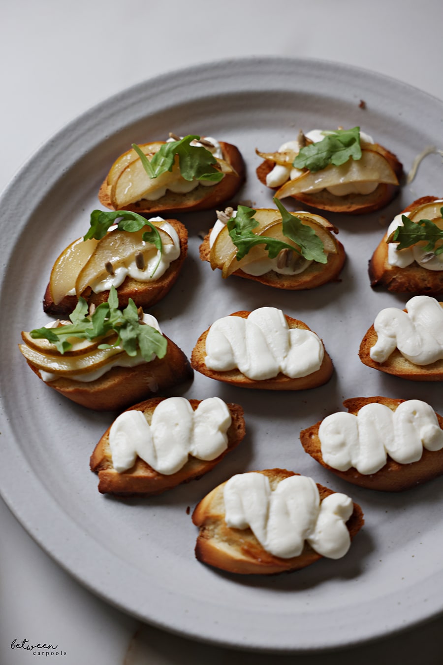 Bruschetta with ricotta cream, roasted pear slices, sunflower seeds, a drizzle of honey, and springs of arugula.