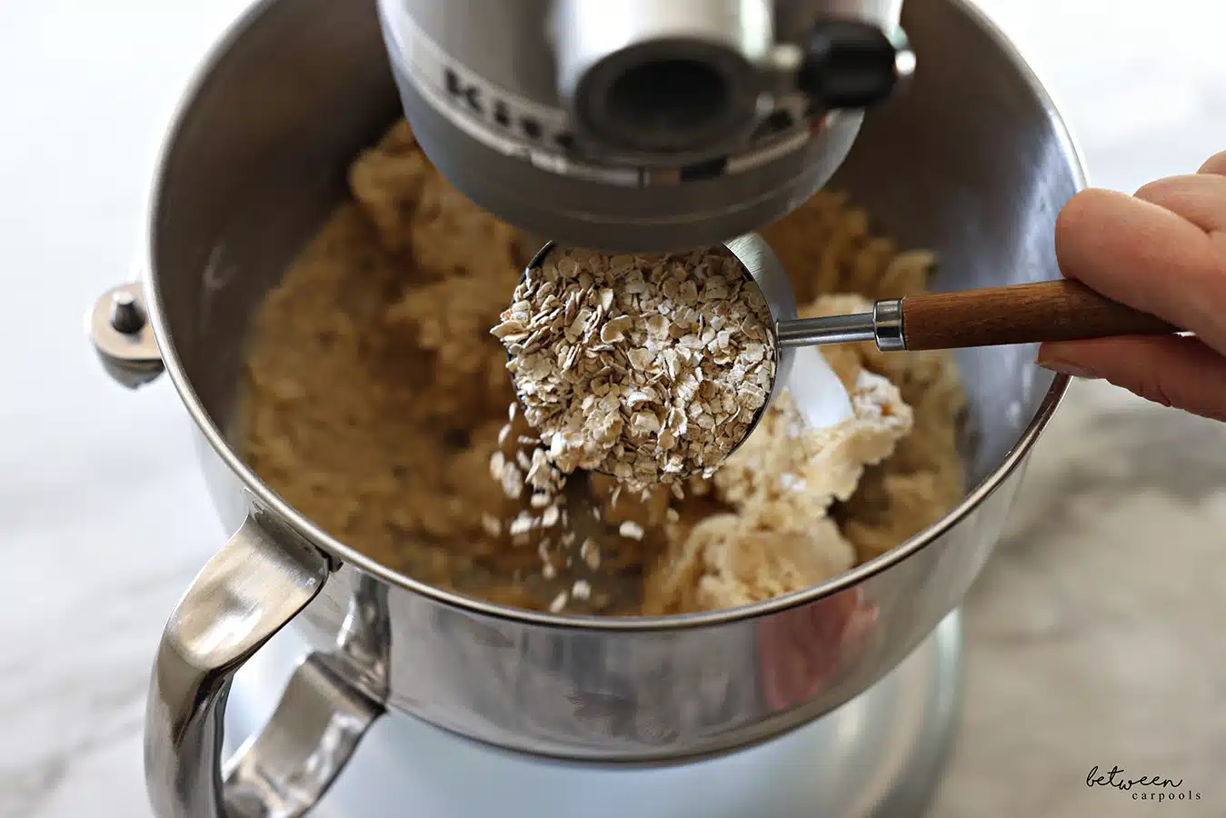 Adding oats to cookie dough in the metal bowl of a Kitchen Aid mixer with the flat beater.