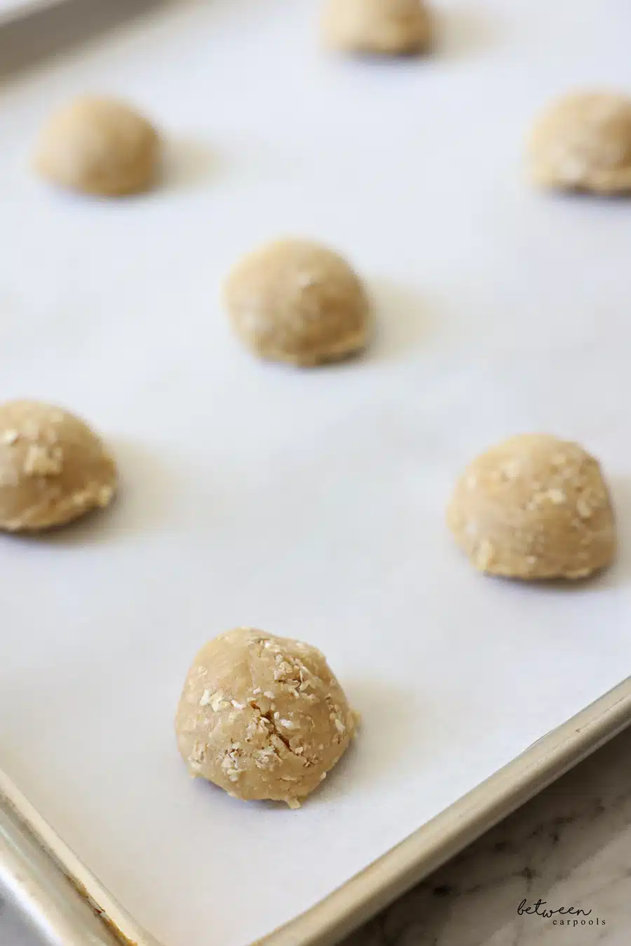 Balls of cookie dough on a parchment lined baking sheet.