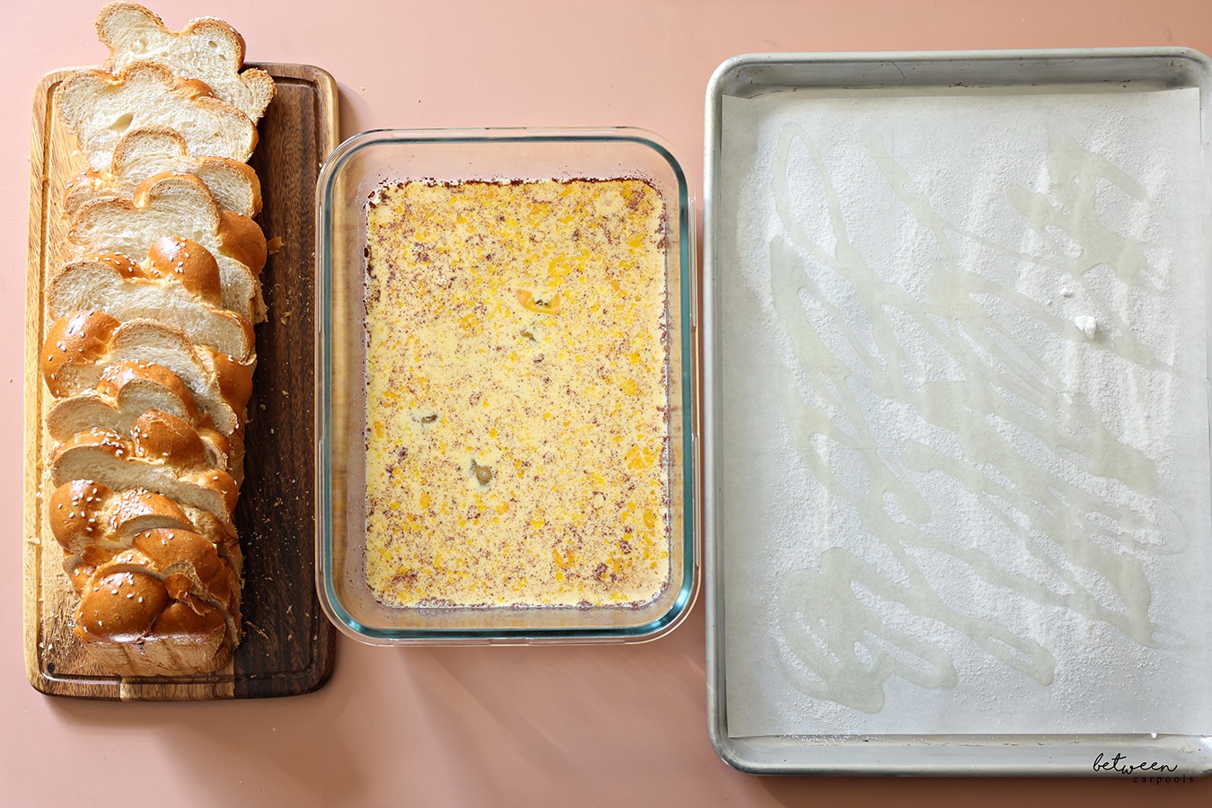 Sliced challah on a wooden board, French toast batter in a glass dish, and a parchment lined baking sheet drizzled with oil and sugar.