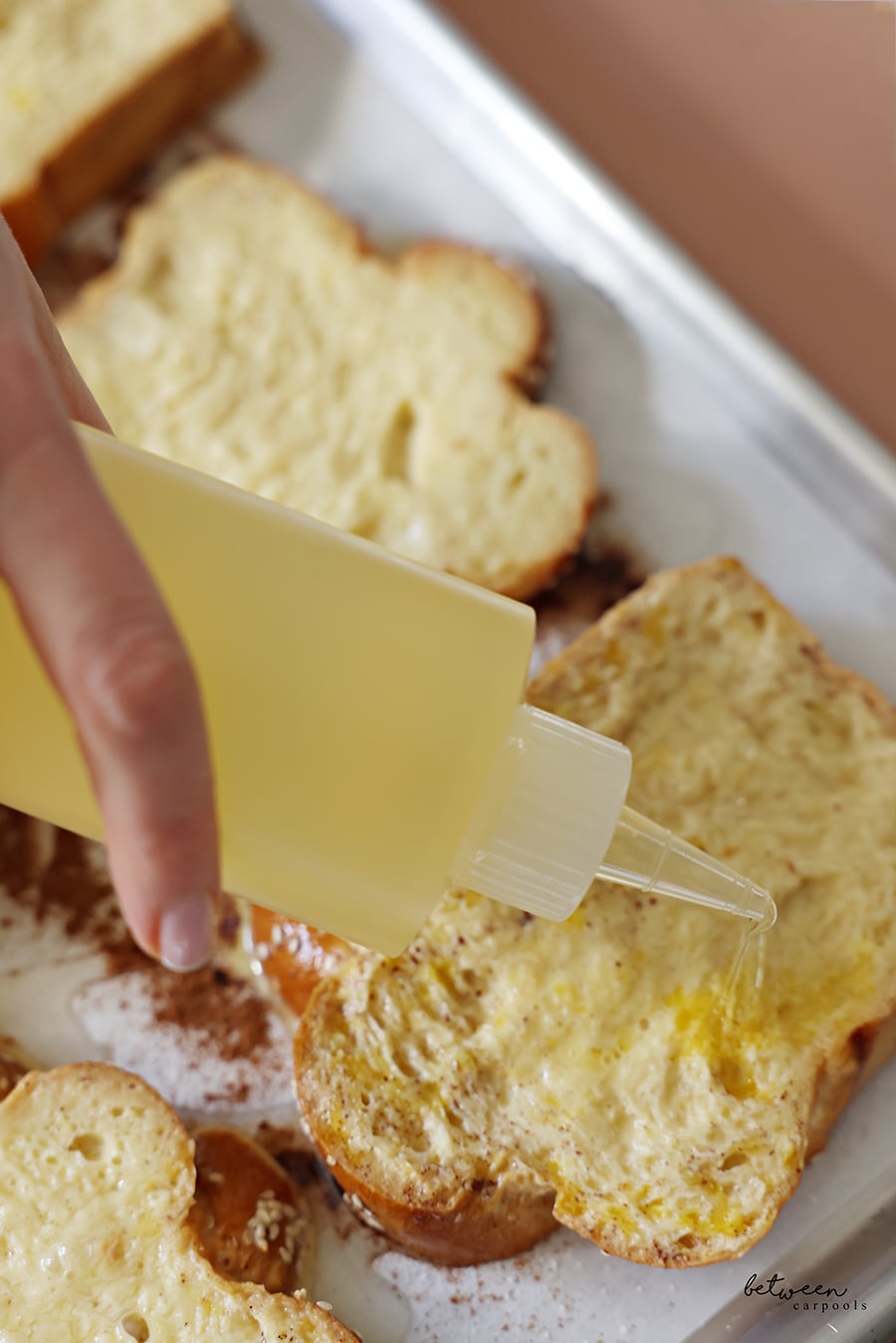 Drizzling oil on slices of challah dipped in French toast batter on a parchment lined baking sheet drizzled with oil and sugar.