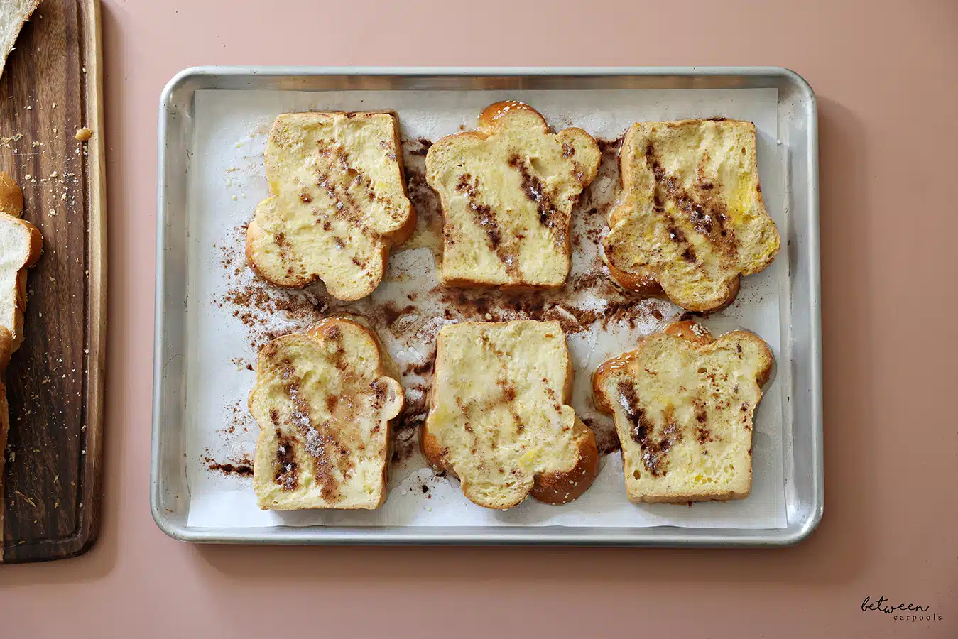 Slices of challah dipped in French toast batter on a parchment lined baking sheet drizzled with oil, sugar and cinnamon.