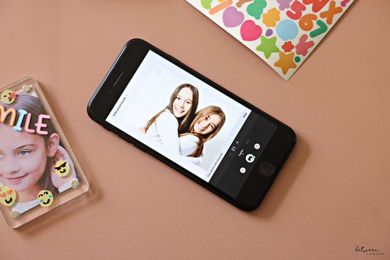 A decorated acrylic frame with a printed photo, an iPhone, and stickers.