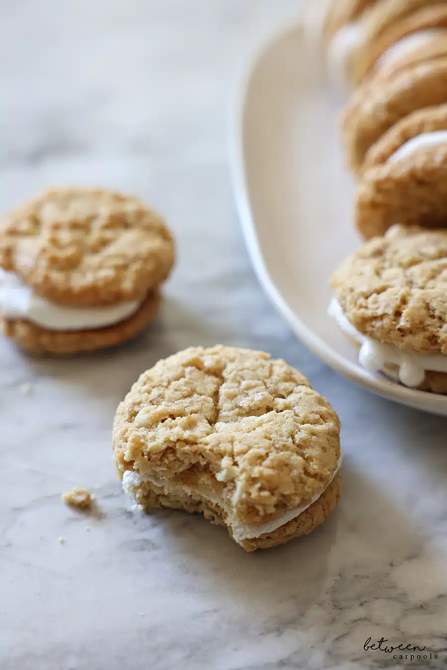 Closeup of one Toasted Marshmallow Sandwich Cookie bitten into. Toasted Marshmallow Sandwich Cookies on a white oval tray in the background.