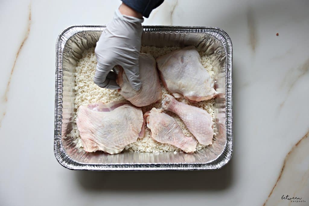 Placing chicken legs, cut in half, into a 9x13 aluminum pan with rinsed raw rice.