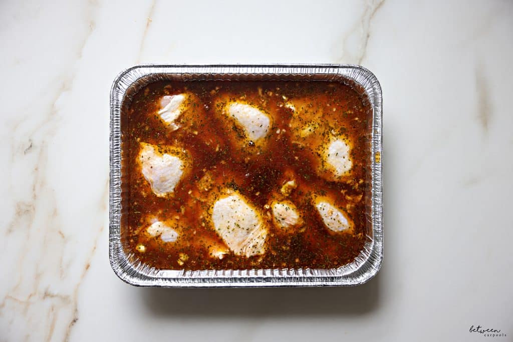 A 9x13 aluminum pan with rinsed raw rice, chicken legs cut in half, and sauce.