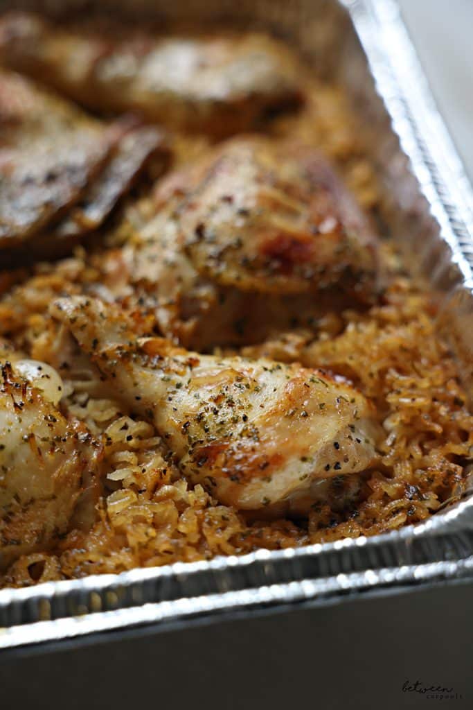 Closeup of baked chicken with rice in a 9x13 aluminum pan.
