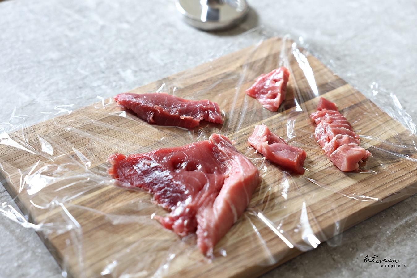 Pieces of fresh tuna on a wooden cutting board covered with plastic wrap.
