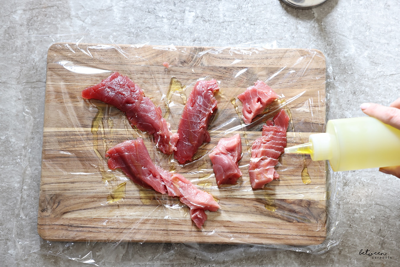 Drizzling olive oil over pieces of fresh tuna on a wooden cutting board covered with plastic wrap.