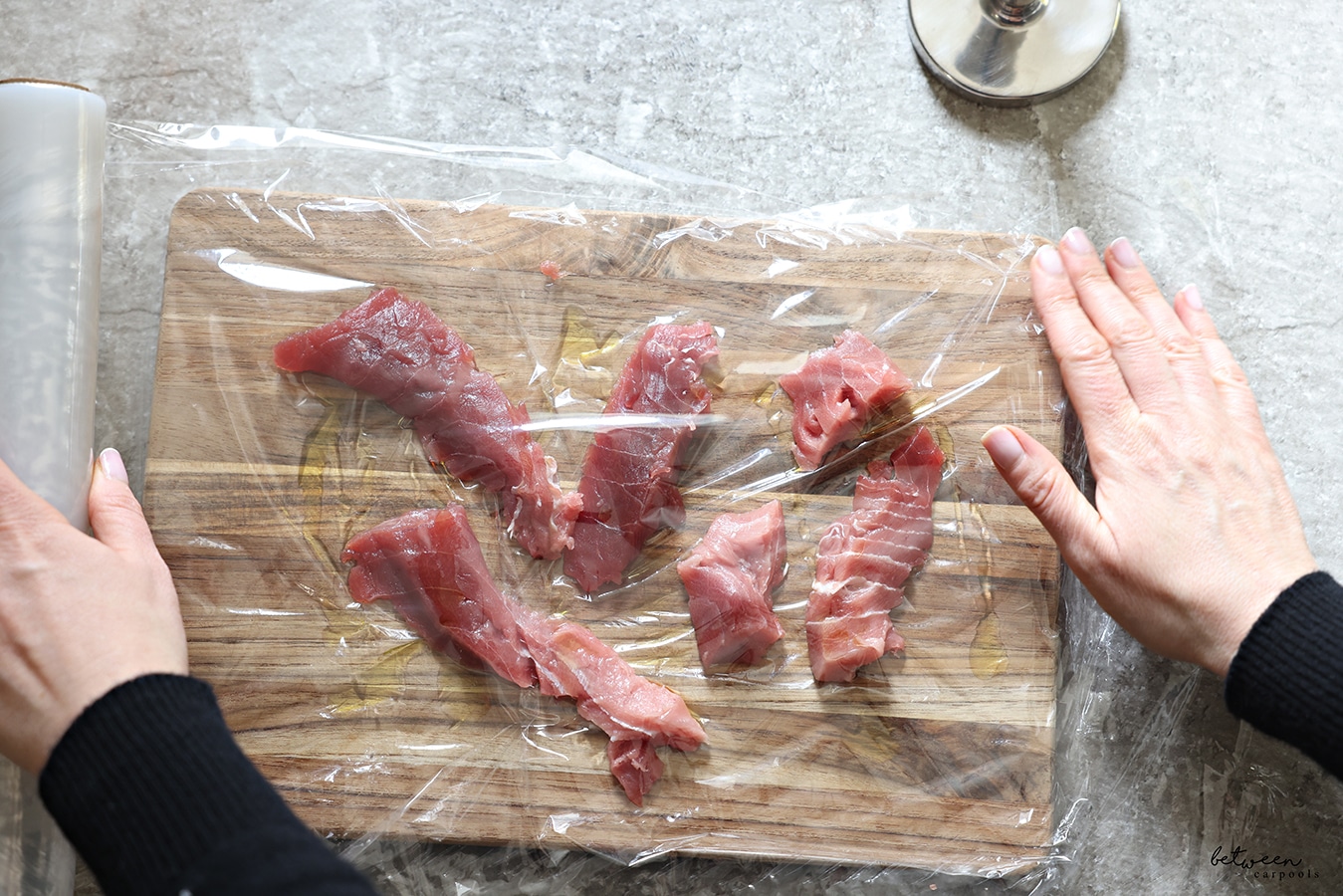 Covering pieces of fresh tuna and olive oil on a wooden cutting board covered with plastic wrap, with another layer of plastic wrap.