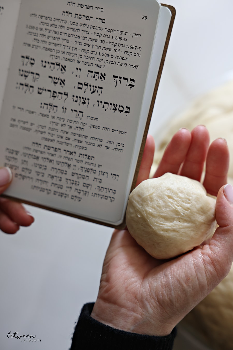 Holding the prayer of Hafrashas Challah in her left hand and a separated piece of challah in her right hand.