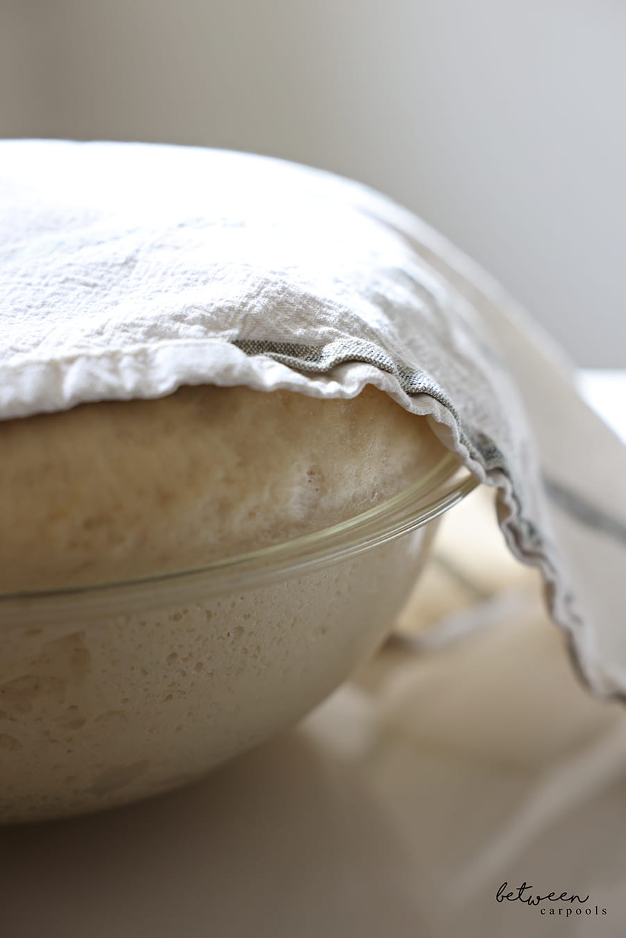 Challah dough rising in a Pyrex glass mixing bowl, covered with a kitchen towel.