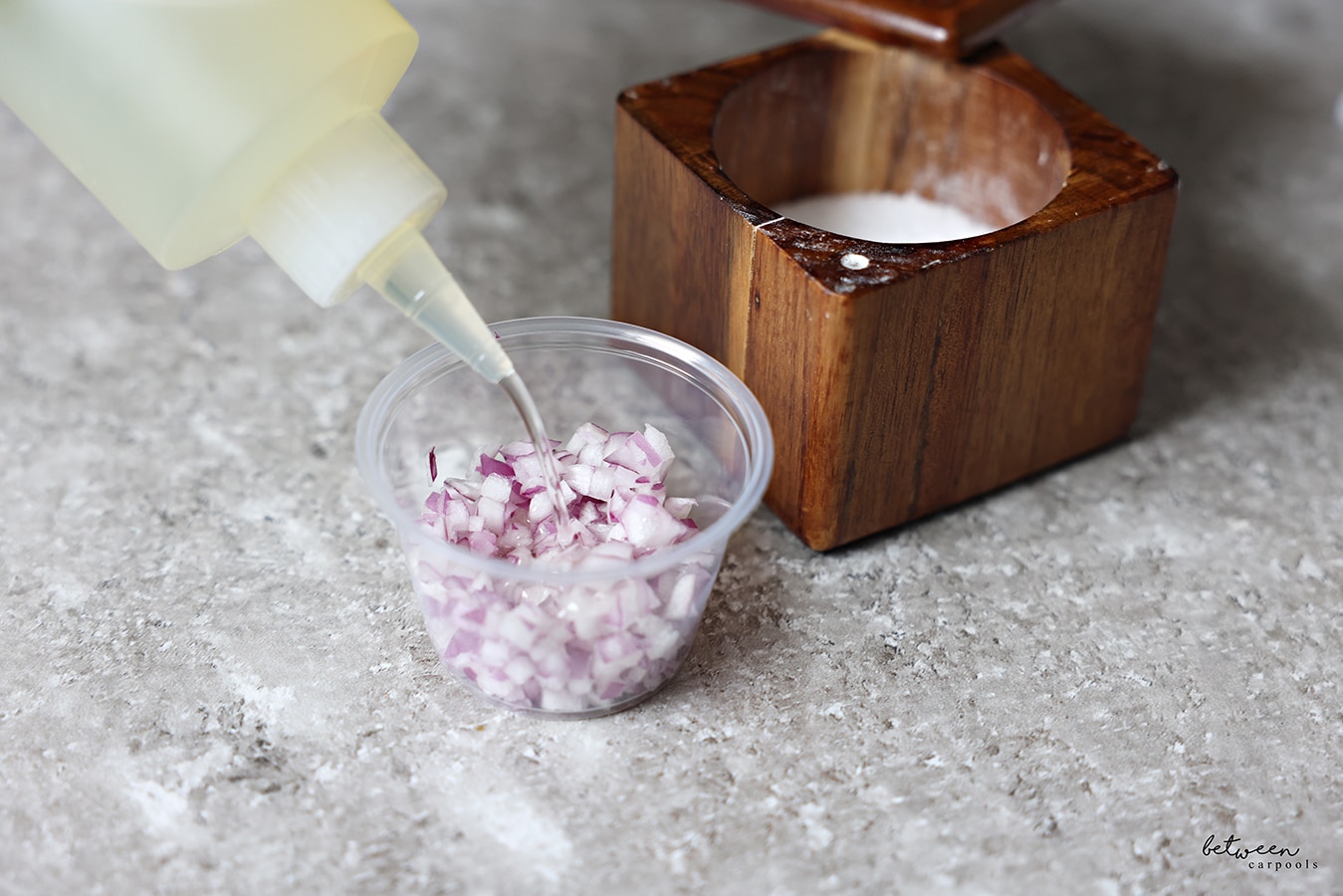 Adding olive oil to a condiment cup with diced red onion. Salt cellar nearby.