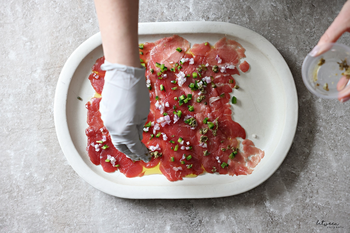 Adding diced capers to diced jalapeño and red onion over the surface of the tuna with olive oil on the serving plate.