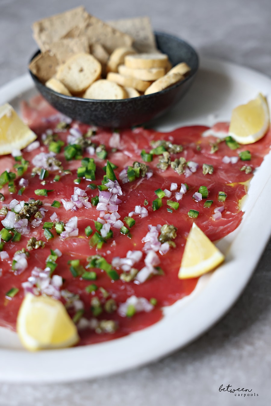 Closeup of tuna carpaccio. with lemon wedges and a bowl of crackers.